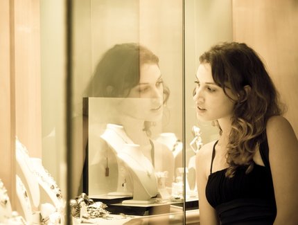 Junge Frau schaut in eine Glasvitrine, in der Schmuck ist